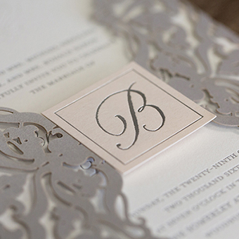 Close up of white and grey invitation with cursive initial. 
